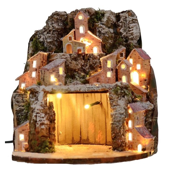 Illuminated snow-covered nativity scene with village and cave