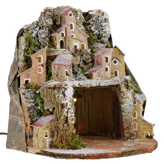 Illuminated snow-covered nativity scene with village and cave