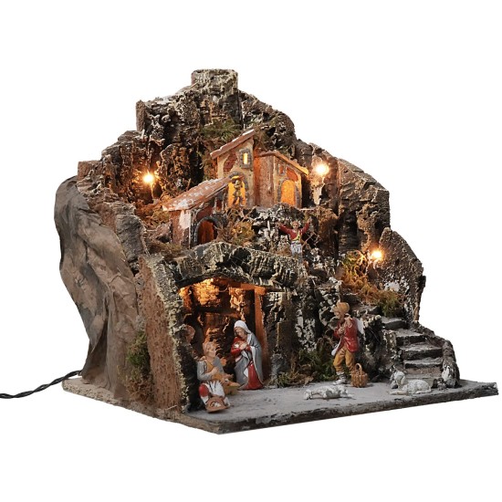 Illuminated nativity scene with village on mountain complete with statues